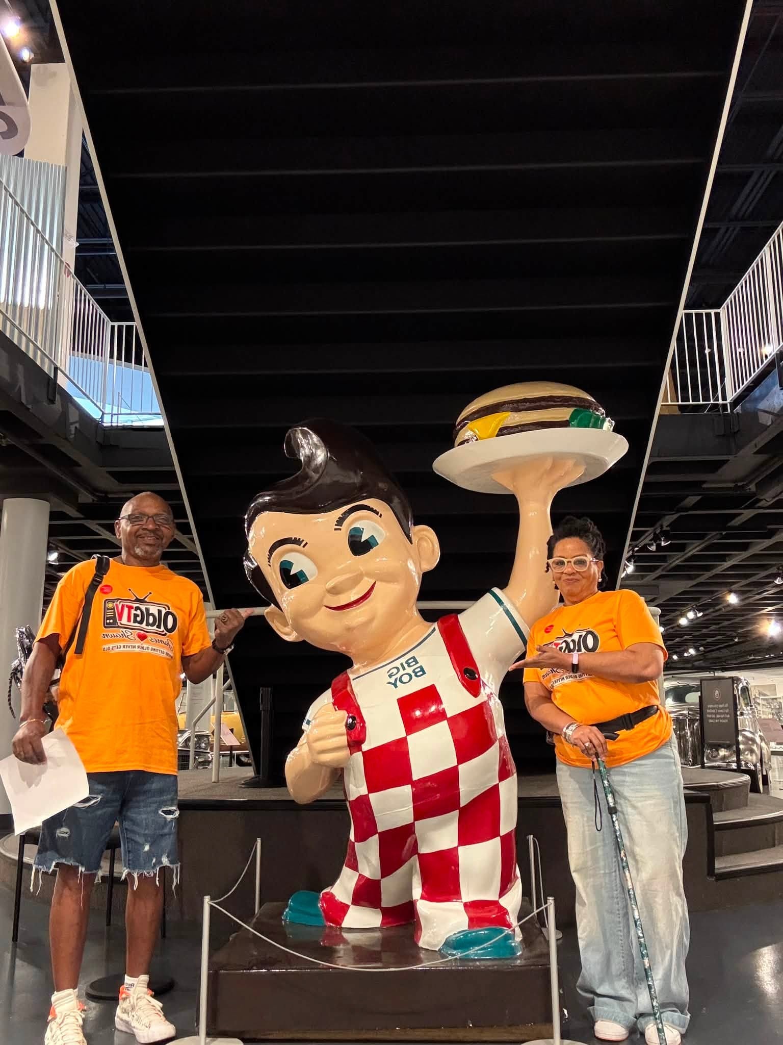 James and Shawn wearing matching orange OLDGTV shirts beside a Big Boy statue